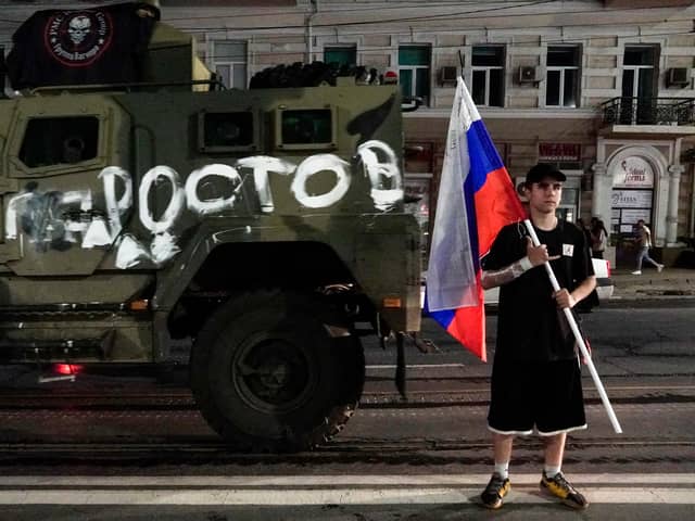 A man holds the Russian national flag in front of a Wagner group military vehicle with the sign read as "Rostov" in Rostov-on-Don late on June 24, 2023. Rebel mercenary leader Yevgeny Prigozhin who sent his fighters to topple the military leaders in Moscow will leave for Belarus and a criminal case against him will be dropped as part of a deal to avoid "bloodshed," the Kremlin said on June 24. (Photo by STRINGER / AFP) (Photo by STRINGER/AFP via Getty Images)