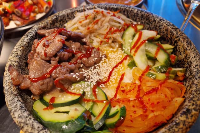 Stone bowl of rice with beef, egg, pickled cucumber, carrots, beansprouts and courgette.
