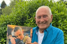 Tommy Cannon holds a photo of himself hugging Robbie Williams.