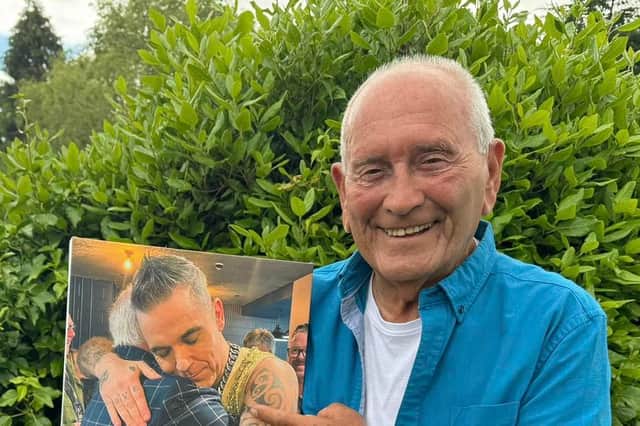 Tommy Cannon holds a photo of himself hugging Robbie Williams.