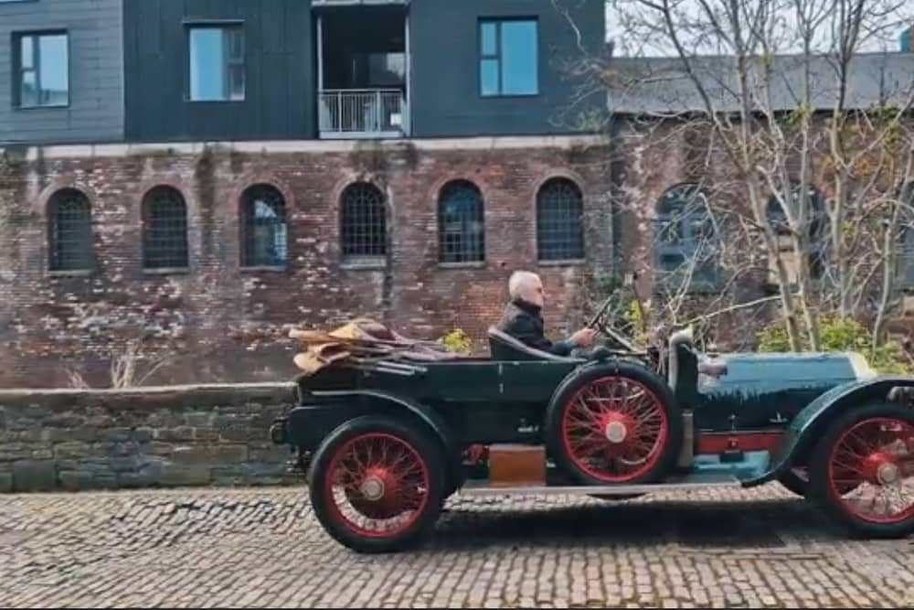 An antique car driving down a cobbled street