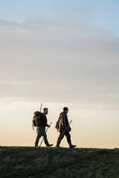 Two figures cross the Ribble Estuary's marshes at dusk. The area's wildfowling traditions are explored in the documentary Call of the Marsh