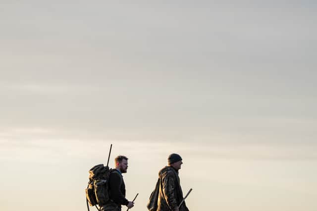 Two figures cross the Ribble Estuary's marshes at dusk. The area's wildfowling traditions are explored in the documentary Call of the Marsh