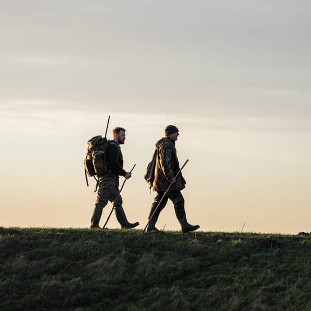 Two figures cross the Ribble Estuary's marshes at dusk. The area's wildfowling traditions are explored in the documentary Call of the Marsh