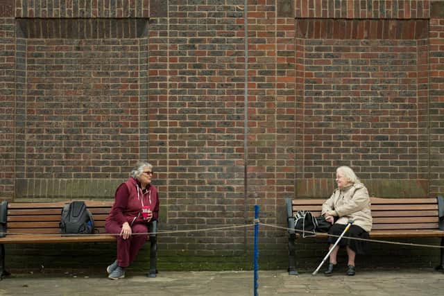 Two women observe social distancing measures as they speak to each other from adjacent park benches amidst the novel coronavirus COVID-19 pandemic