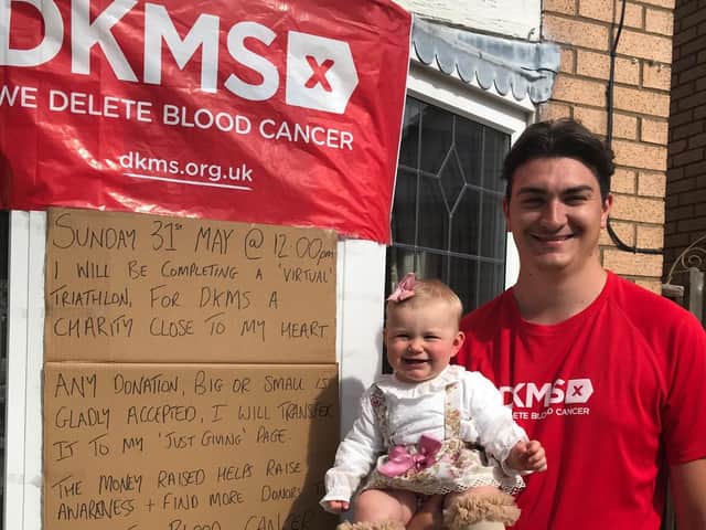 Alex and daughter, nine month old Pearl Lily, pictured by a poster and banner promoting the triathlon from home