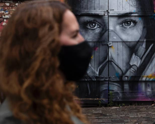 A woman wearing a face mask walks past a mural of a woman wearing a mask
