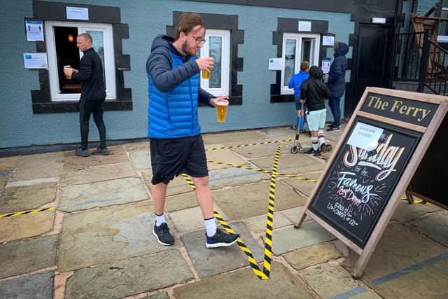 Customers carry their take-away draught beer served in plastic cups, outside 'The Ferry' pub, overlooking the river Mersey in Egremont, on the Wirral Peninsula  (Photo by PAUL ELLIS/AFP via Getty Images)