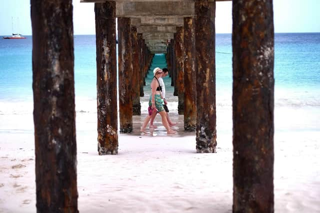 Two tourist walk under a jetty as they stroll along a beach in Bridgetown, Barbados