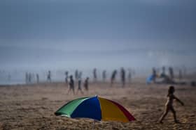 An umbrella stands on the sand as beachgoers enjoy a day at Costa da Caparica beach in Almada