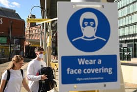 Pedestrians walk past a sign urging people to 'wear a face covering' due to the COVID-19 pandemic, in Manchester (Photo by OLI SCARFF/AFP via Getty Images)