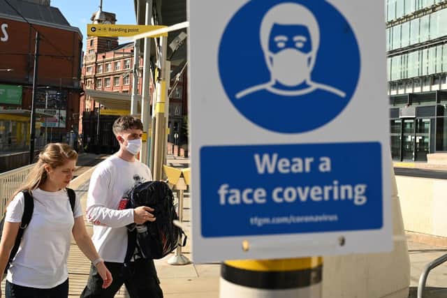 Pedestrians walk past a sign urging people to 'wear a face covering' due to the COVID-19 pandemic, in Manchester (Photo by OLI SCARFF/AFP via Getty Images)