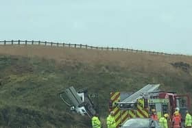 Pictures from the scene show a white car on its roof on a grass embankment next to the road