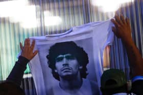 Fans hold a jersey with the face of Diego Maradona at Clínica Olivos on November 03, 2020 in Olivos, Argentina. Personal doctor of Maradona, Leopoldo Luque, confirmed the former footballer was to undergo surgery to treat a clot in his brain