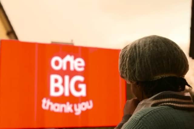 The big screen says 'One Big Thank You' to Glenda for her work with the Windrush community.