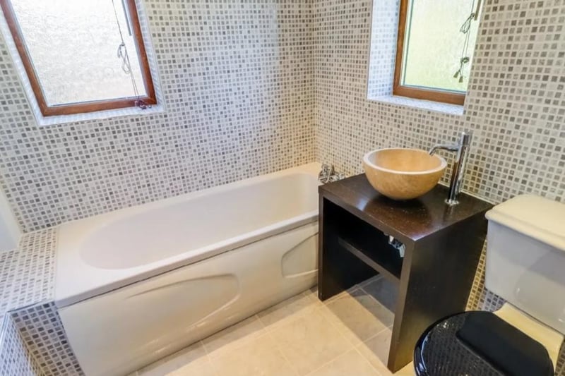 Three piece suite comprising low flush w.c., vanity shelving with a stone circular wash basin having a chrome mixer filler, panelled bath with chrome mixer tap, partially tiled walls, tiled floor with underfloor heating.
