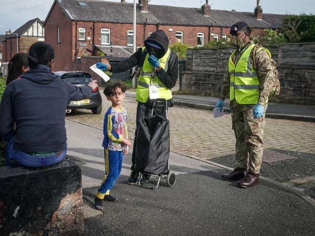 Children play in the street as gunners from the Royal Horse Artillery distribute Covid-19 polymerase chain reaction (PCR) tests to local residents in Bolton