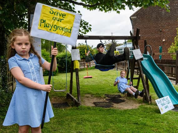 Darcy McNab holds a protest sign whilst Jacques Chamberlain and Evie Lilley ride the swings which are to be pulled down.