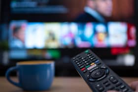 Netflix remote control with TV behind in evening with Netflix menu (Shutterstock)