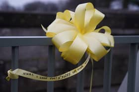 A yellow ribbon with a message of hope written on it is tied to a bridge over the River Wyre in St Michael's