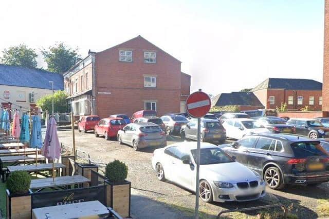 The car park where the flats will be built and, to the left, tables and chairs from the neighbouring Rose and Crown pub, laid out on the currently closed stretch of Dole Lane (image: Google)