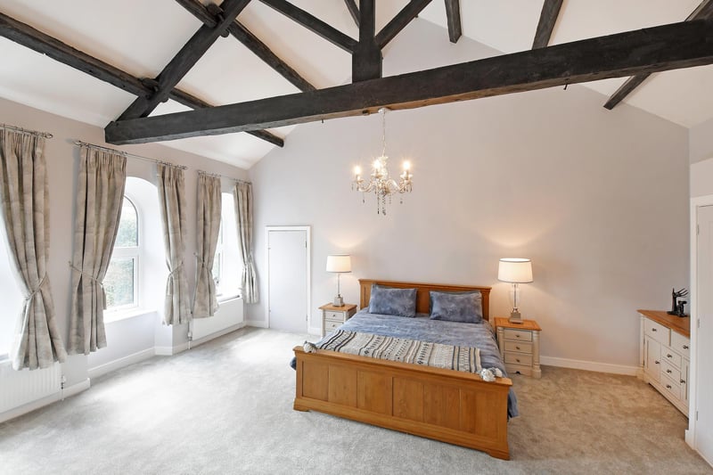 A grand master bedroom with the focal points being the stunning vaulted ceiling with exposed timber beams and front facing arched UPVC double glazed windows. There’s a range of fitted furniture, incorporating short hanging and shelving.