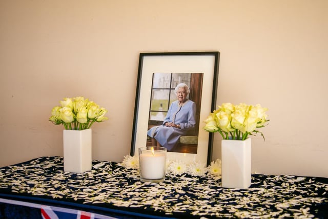 Flowers and lit candles placed by a picture of the Queen in memory of her many years of service.