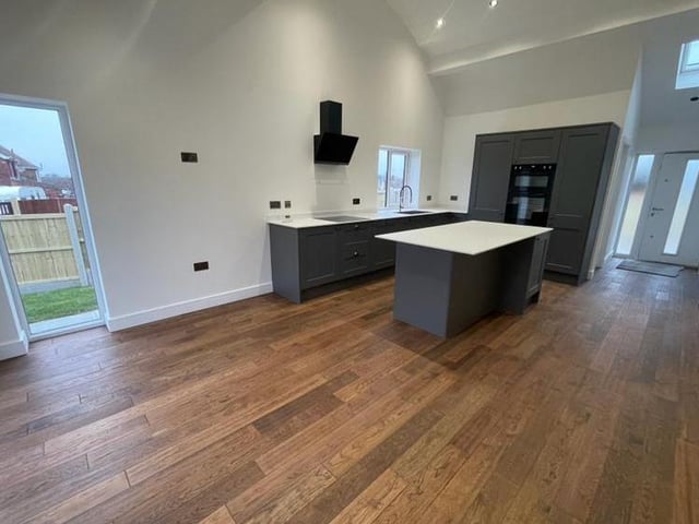 Another view of the open-plan dining kitchen and living area. There is an electric induction hob with extractor hood over, a  central island, inset spotlights to the ceiling and a range of modern Edwardian-style radiators, some traditional, some vertical.