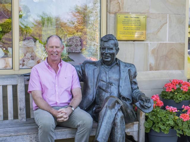 Guy sitting with the statue of his late father that's situated at the front of the garden centre