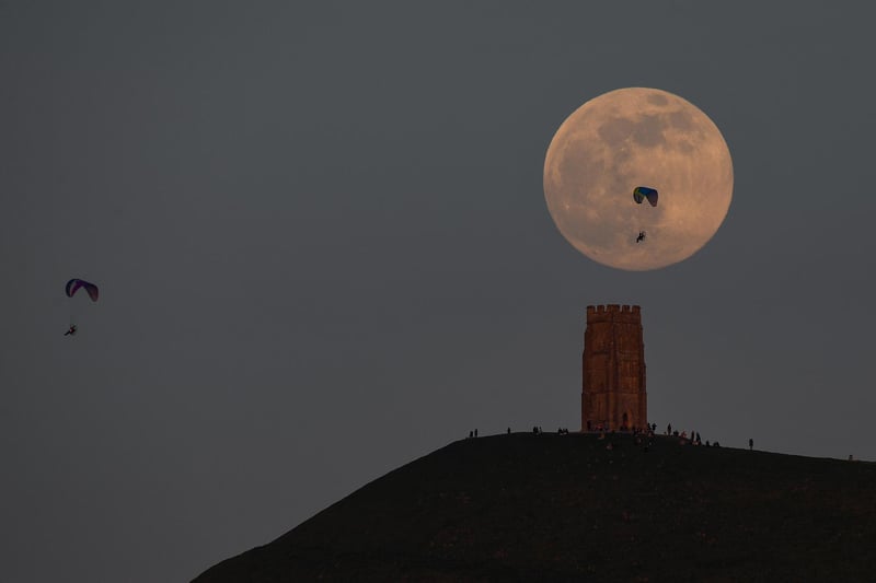 Paragliders are seen as the full moon rises behind Glastonbury Tor (Photo by Finnbarr Webster/Getty Images)