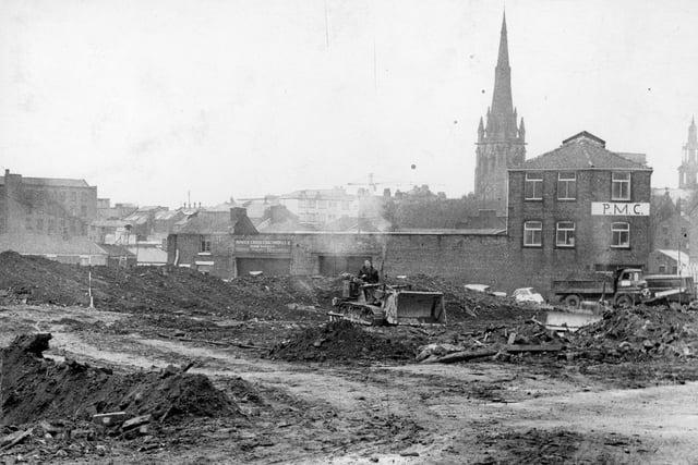 In this undated image you can see the spire of St Walburge's Church to the right, behind the PMC building and Howick Cross Coachworks in Preston. A worker clears the demolition wreckage