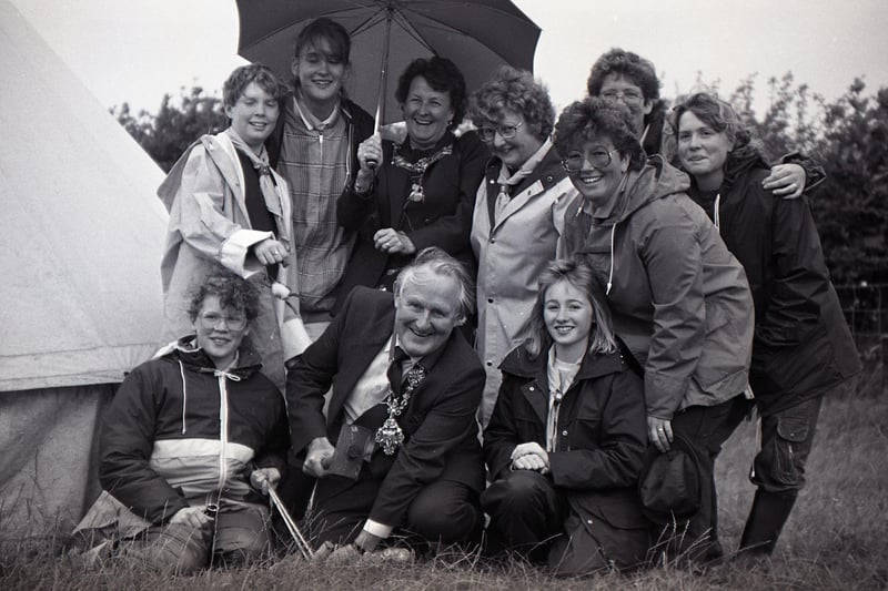 The Mayoress of Preston, Mrs Betty Atkinson, offers shelter to her husband who showed how adept he was at knocking in tent pegs, watched by interested guides as the Lancashire West Girl Guides held their first ever international camp at Guy's Farm, Forton, near Lancaster