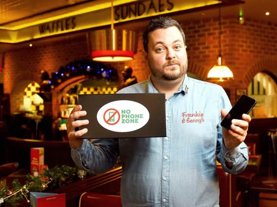 A Frankie & Benny's employee holding a no-phone zone box