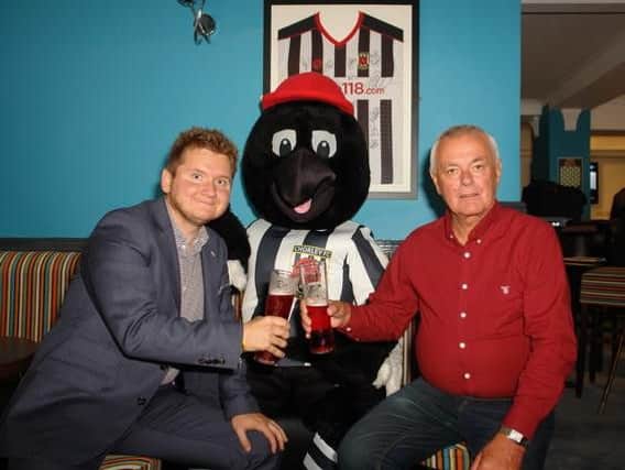 Chorley FCs Josh Vosper (left) and The Crown's owner Frank Smalley celebrate the new club-inspired walls with Chorley FC mascot Victor Magpie