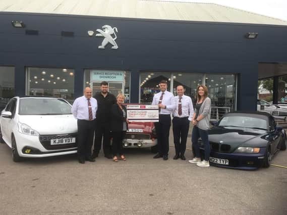 Rosemere Cancer Foundations corporate fund-raising manager Cathy Skidmore, third from the left, is presented with the donation by Robins & Days general manager Antony Georgiou, technician Dean Christopher, who showed his white Peugeot 208 GTI, Nick Green with his red MG BGT, service manager Paul Livsey and Kat Sangster, who showed her BMW Z3