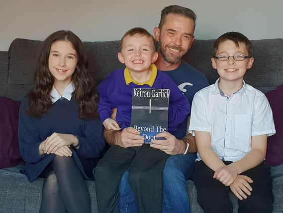 Keiron Garlick, has published a book - Beyond The Door. He is pictured with his three children, Ellie, 13, Nathan, 10, and George, five.