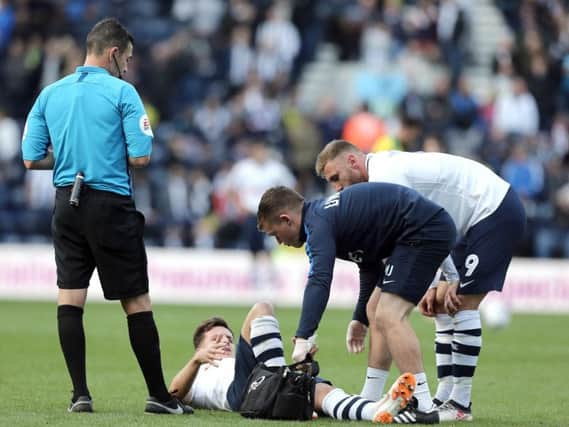 Preston midfielder Josh Harrop is attended to by physio Matt Jackson, watched by team-mate Louis Moult