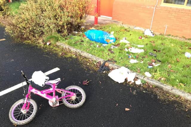 A child's bike has been abandoned and bags of overflowing rubbish are scattered around the car park