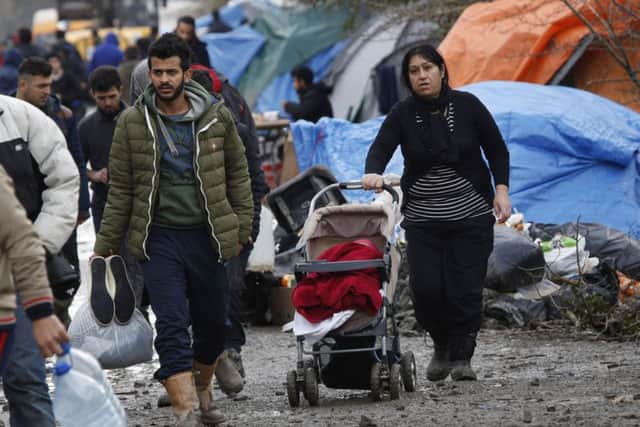 A migrant family walk in the mud in a makeshift camp