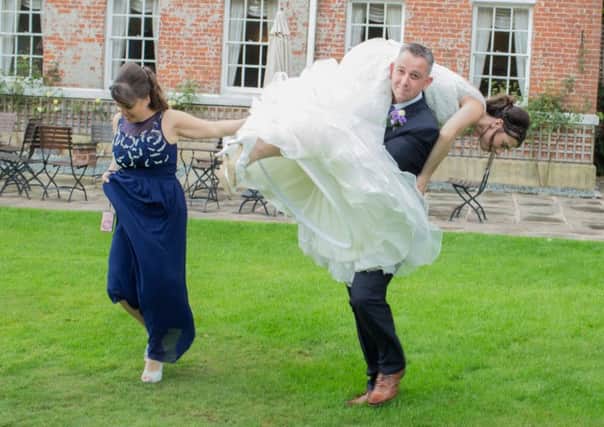 Russell Fowley and Laura Hammond. Russell lifts his bride over his shoulder to take her to the gardens for photos following wind and rain on their wedding day.