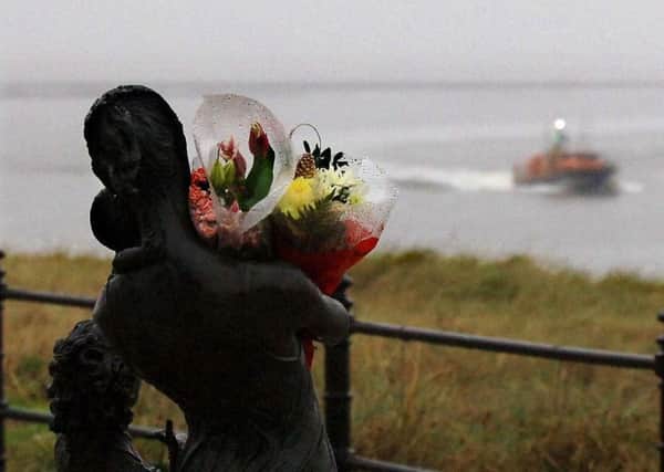 Flowers placed on the Welcome Home statue in the foreground with the Fleetwood lifeboat returning with wreckage from the crashed civil helicopter.