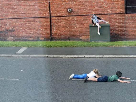 Young children lying down on a busy road and playing chicken