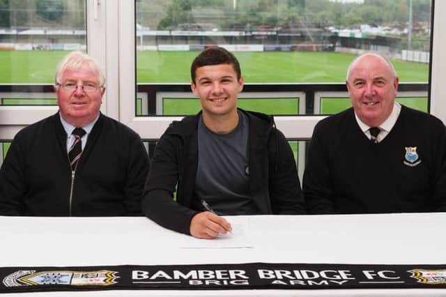 Macauley Wilson signs a contract with Bamber Bridge flanked by club secretary George Helliwell and Frank Doyle