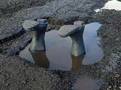 A pair of green welliesare propped up upsidedown with a quip, local resident looking into the pothole problem.