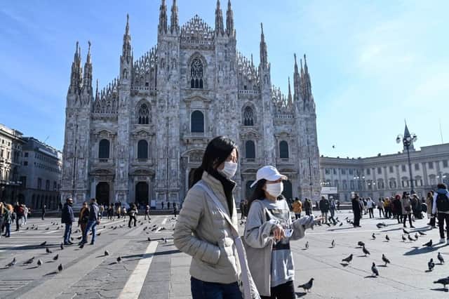 Two women wearing a protective facemask walk across the Piazza del Duomo, in front of the Duomo, in central Milan, on February 24, 2020 